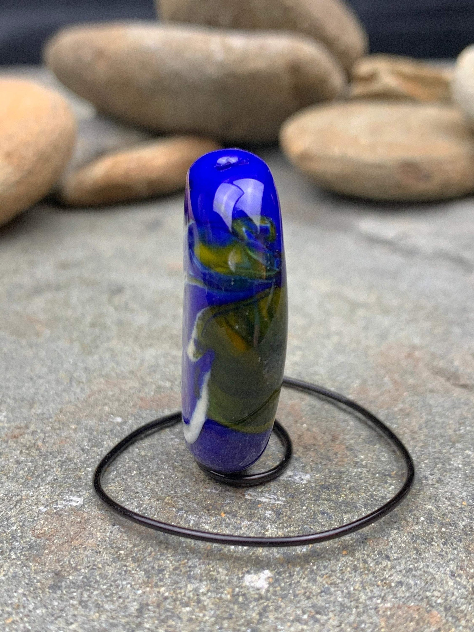 a handmade lampworked glass bead with blue and white dots on a green background