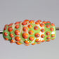 a handmade lampworked glass bead with orange dots on a green and white background