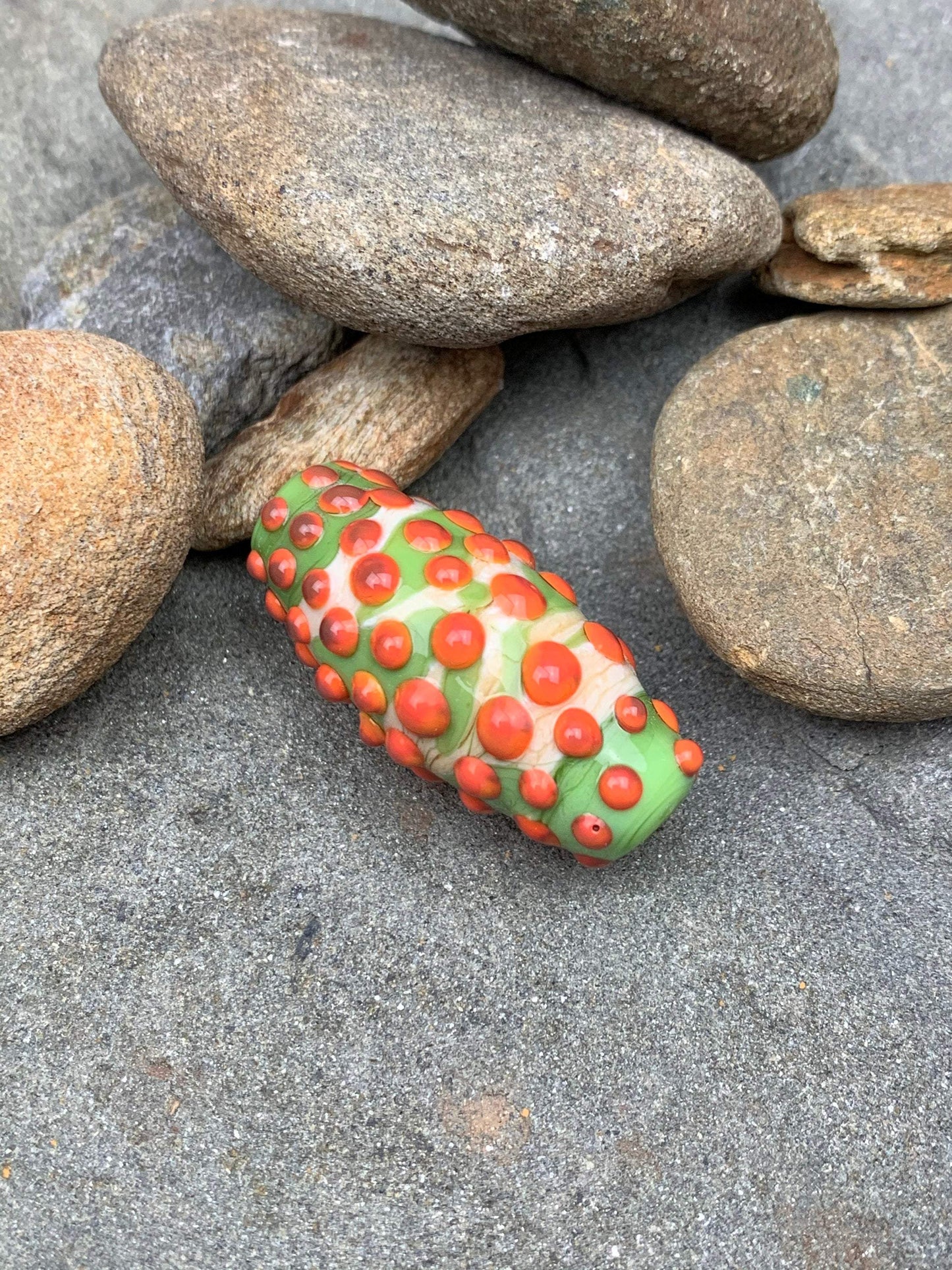 a handmade lampworked glass bead with orange dots on a green and white background