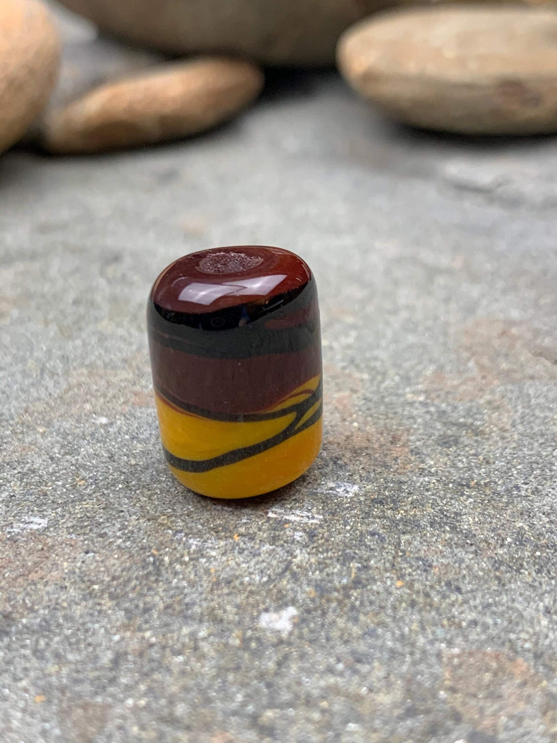 a handmade lampworked glass bead with black stripe on a yellow and brown background