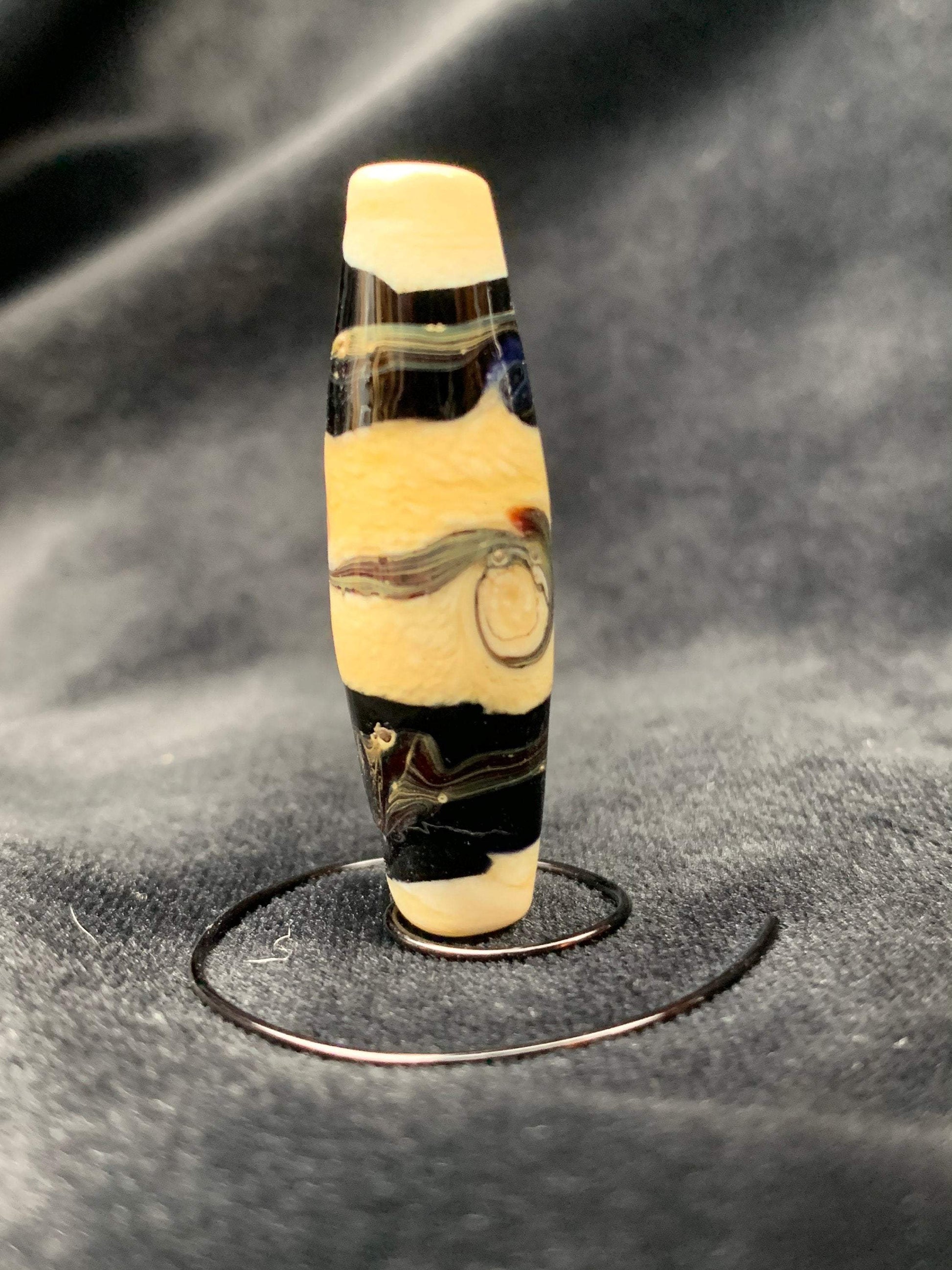 a handmade lampworked glass bead with black stripes and swirls on an ivory background