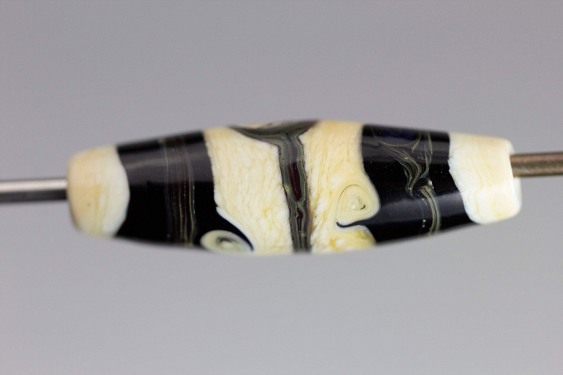a handmade lampworked glass bead with black stripes and swirls on an ivory background