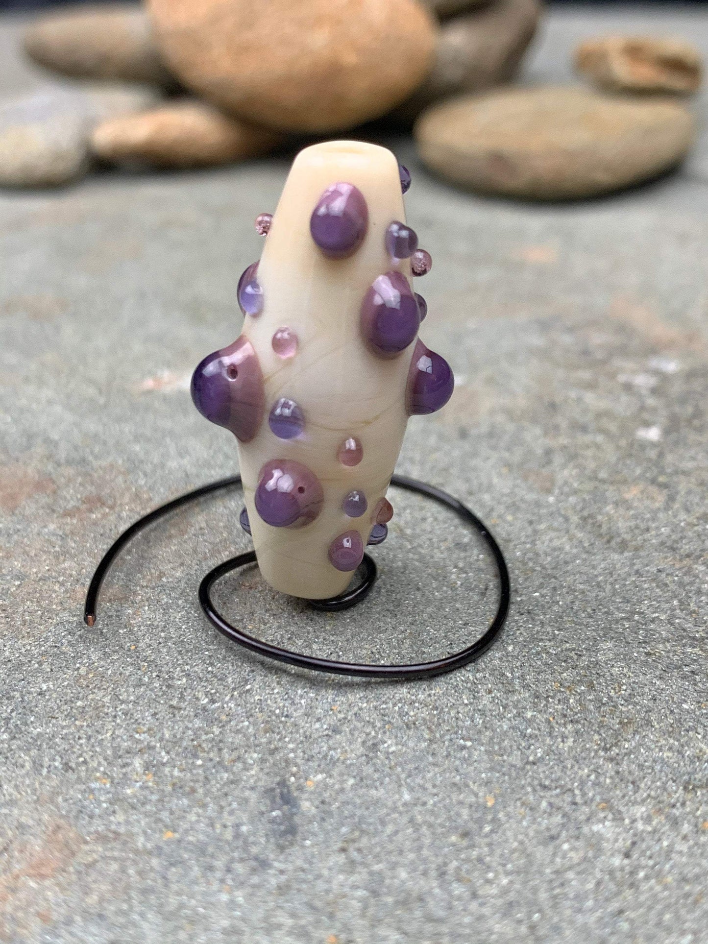 a handmade lampworked glass bead with purple and mauve dots on a white background