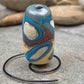 a handmade lampworked glass bead with turquoise and white dots on an ivory and brown background