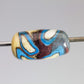 a handmade lampworked glass bead with turquoise and white dots on an ivory and brown background