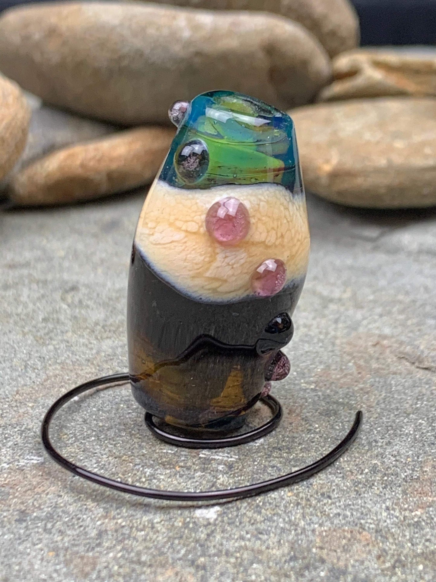 a handmade lampworked glass bead with pink dots on a teal, black and green background