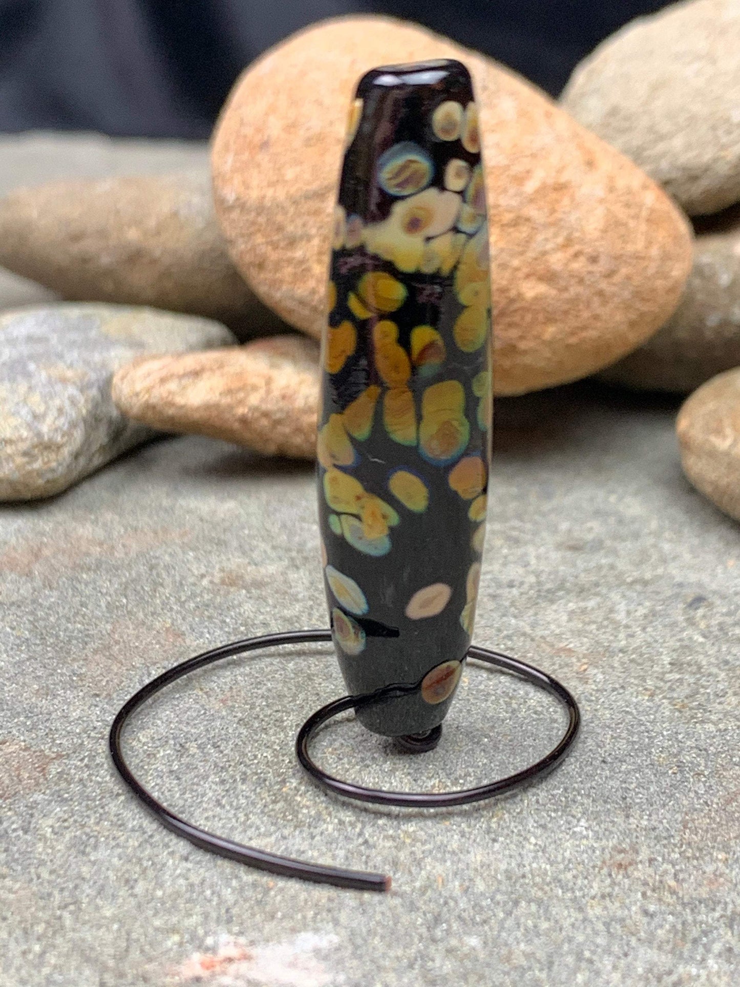 a handmade lampworked glass bead with multicolor dots on a black background