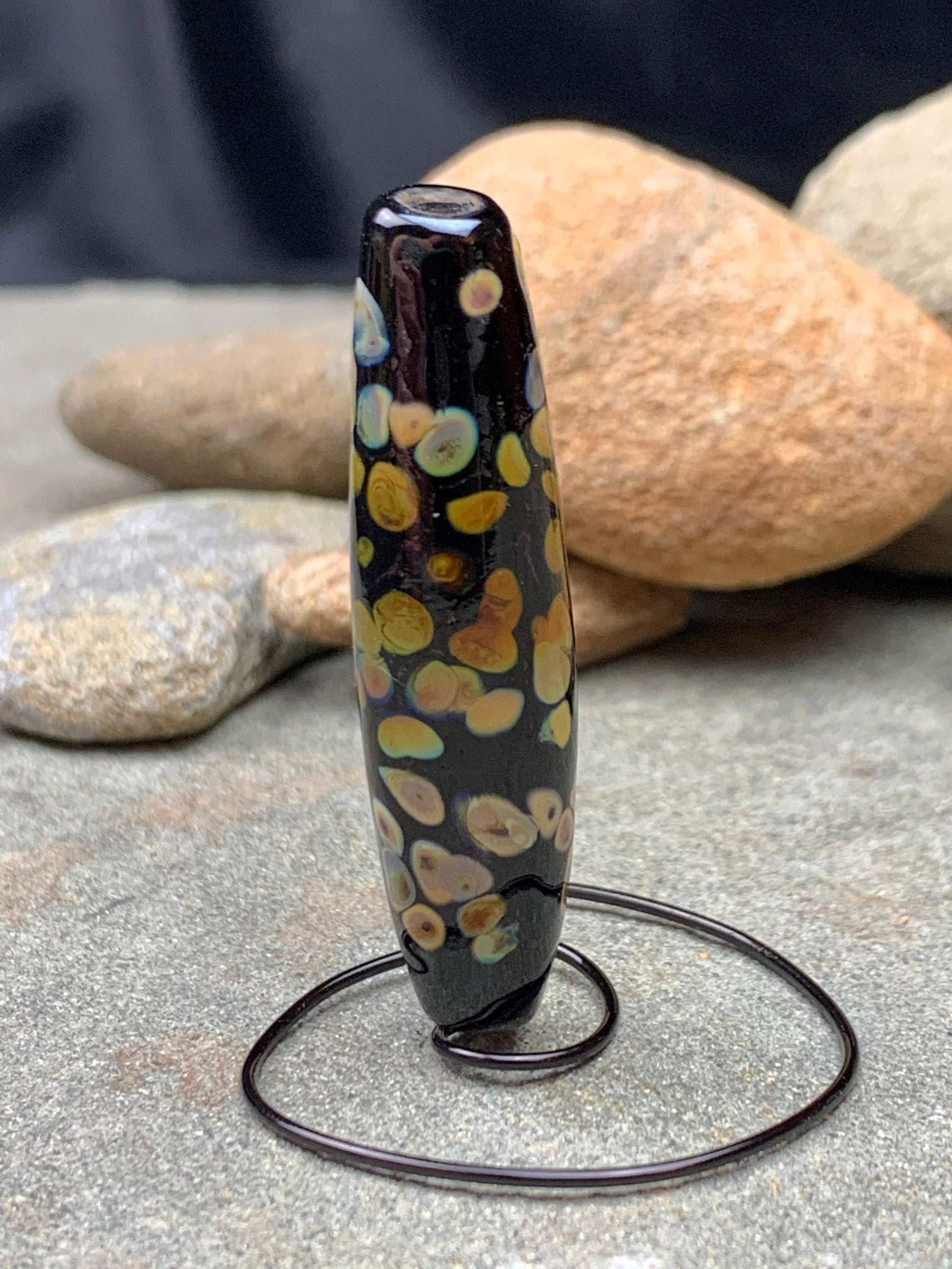 a handmade lampworked glass bead with multicolor dots on a black background