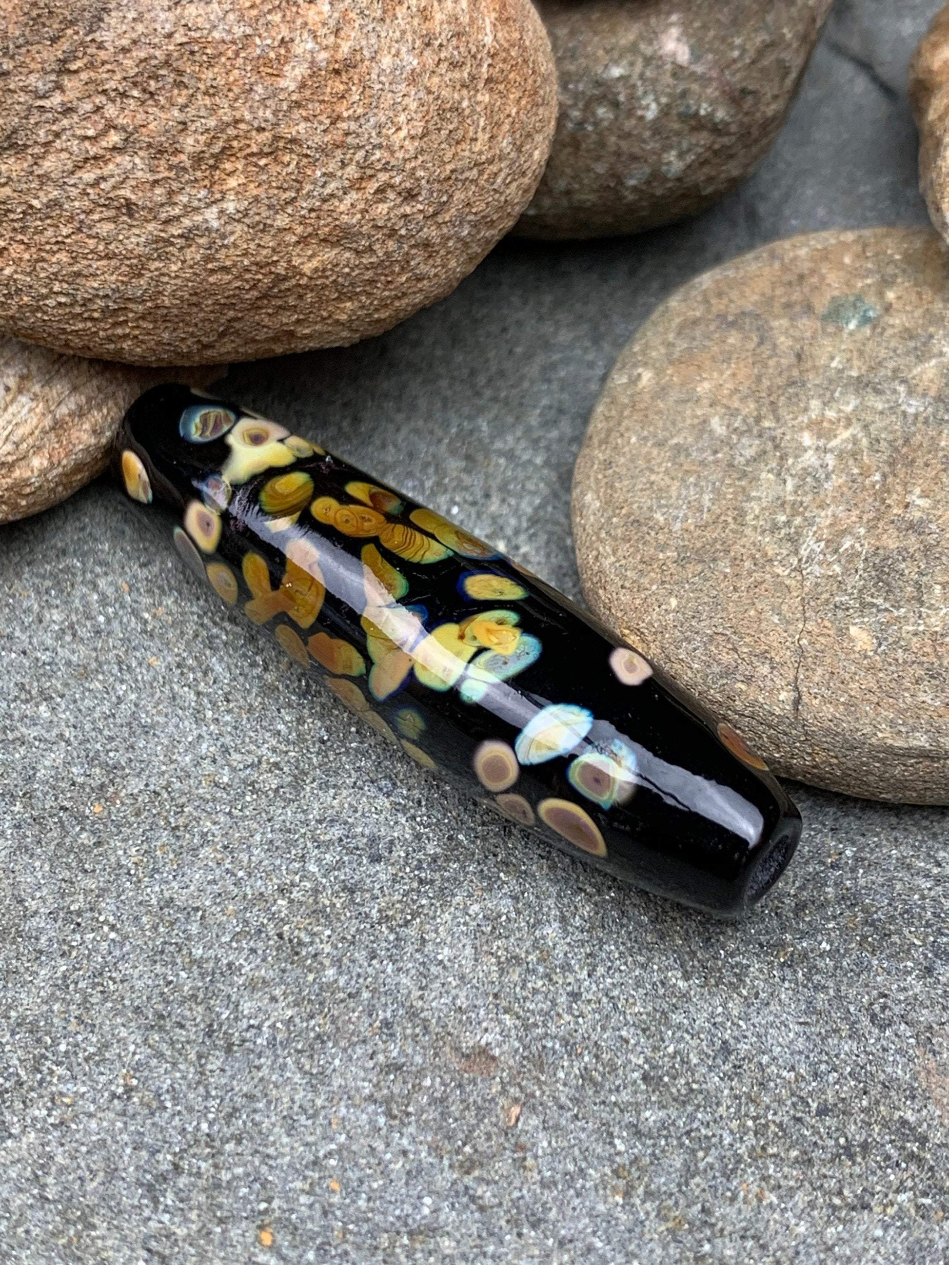 a handmade lampworked glass bead with multicolor dots on a black background