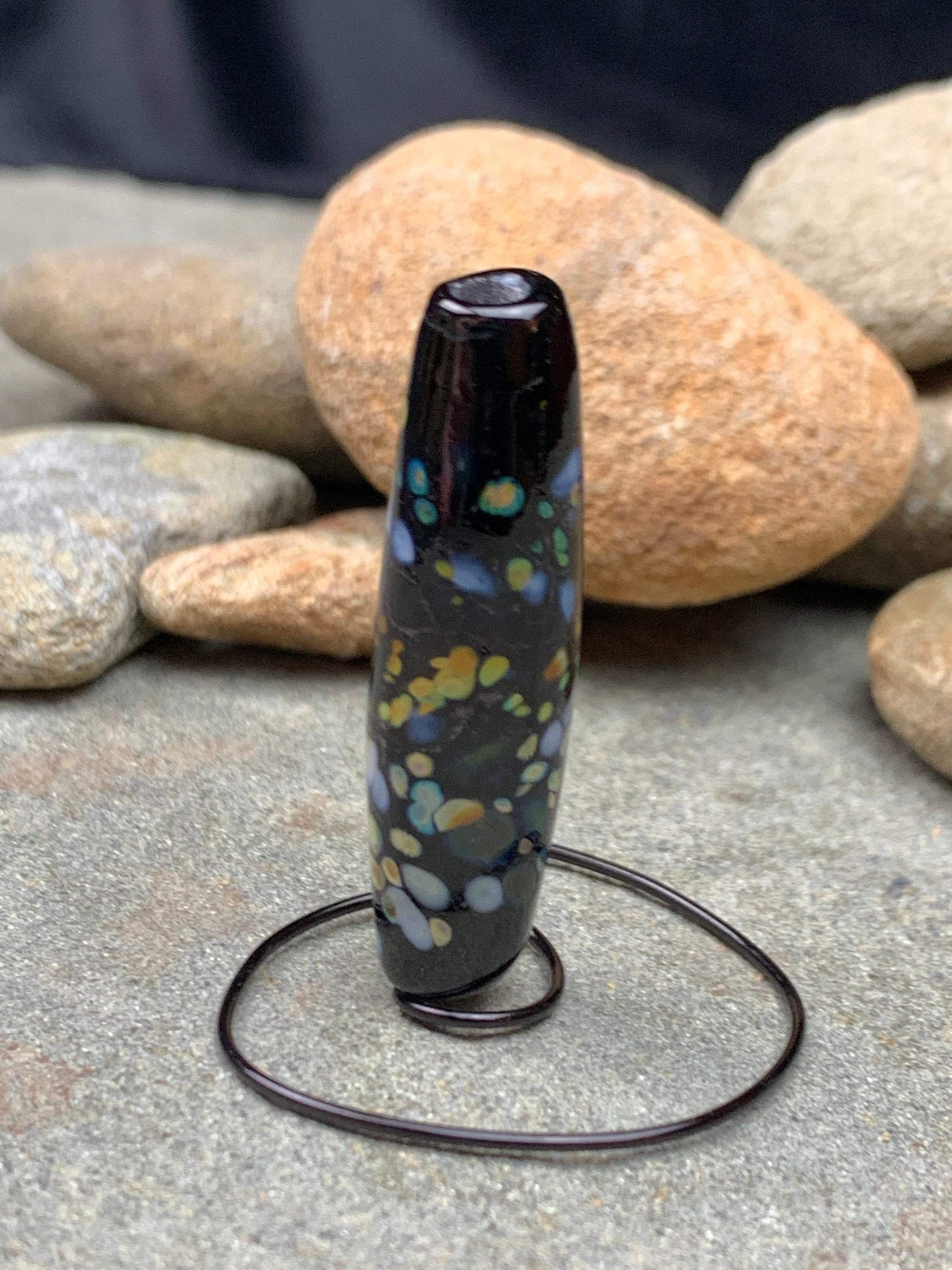 a handmade lampworked glass bead with multicolor dots on a black background