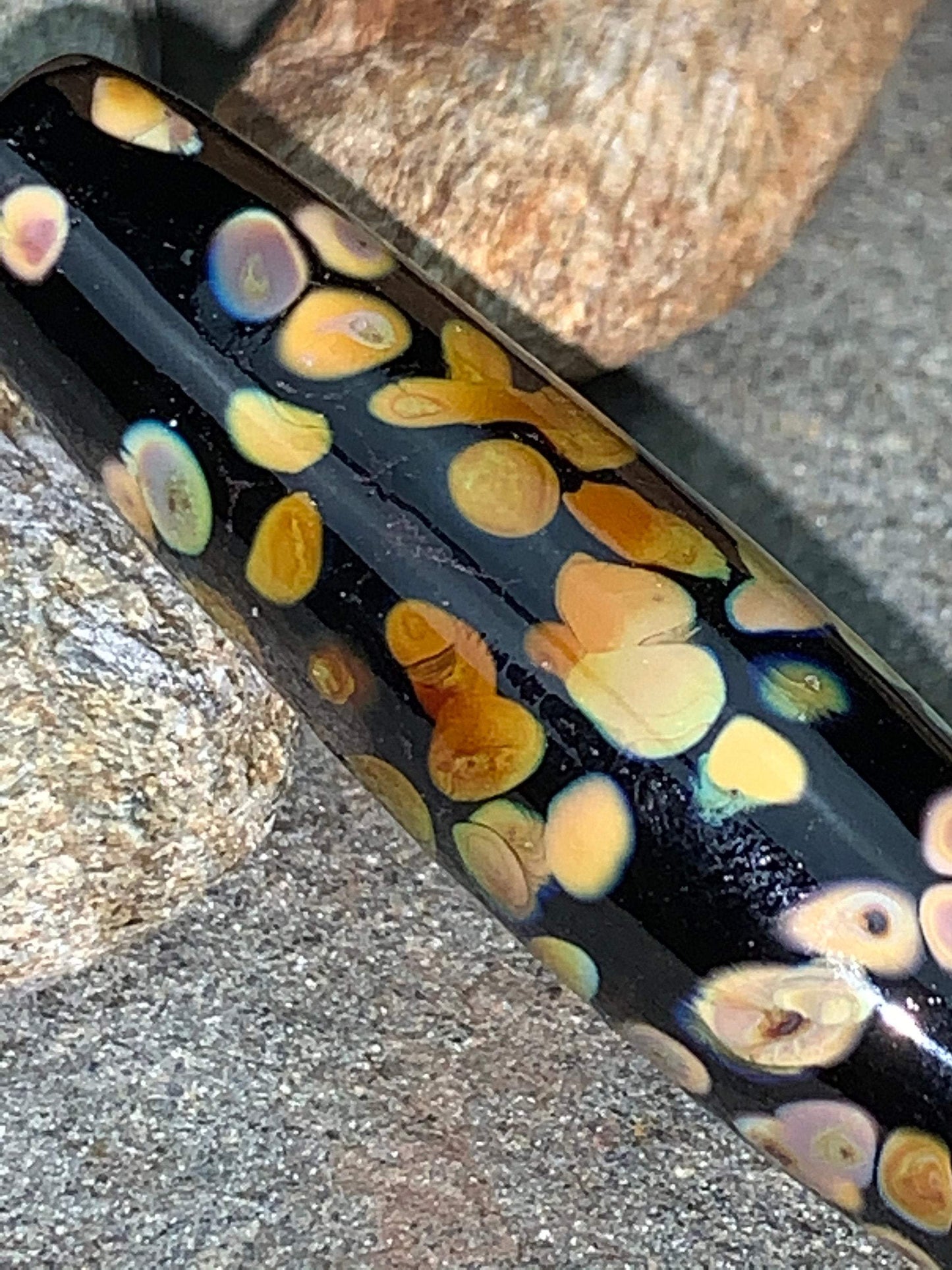 a handmade lampworked glass bead with multicolor dots on a black background
