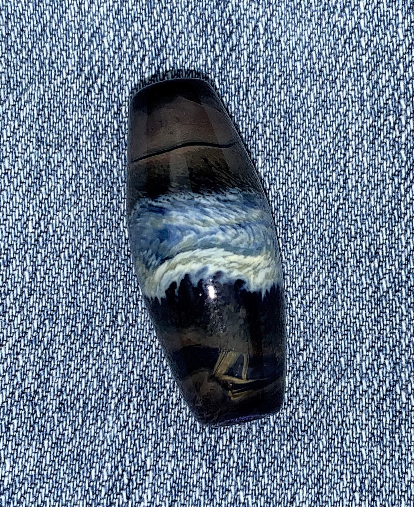 a handmade lampworked glass bead with ivory and light blue bands on a dark blue background