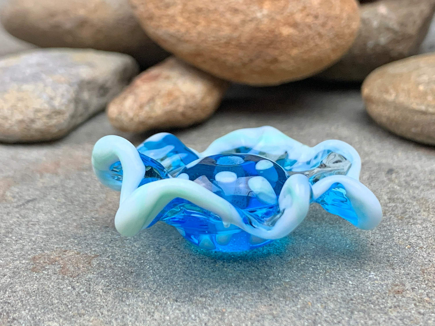 a handmade lampworked blue glass bead with a blue glass ruffle with white dots around the middle of the bead.