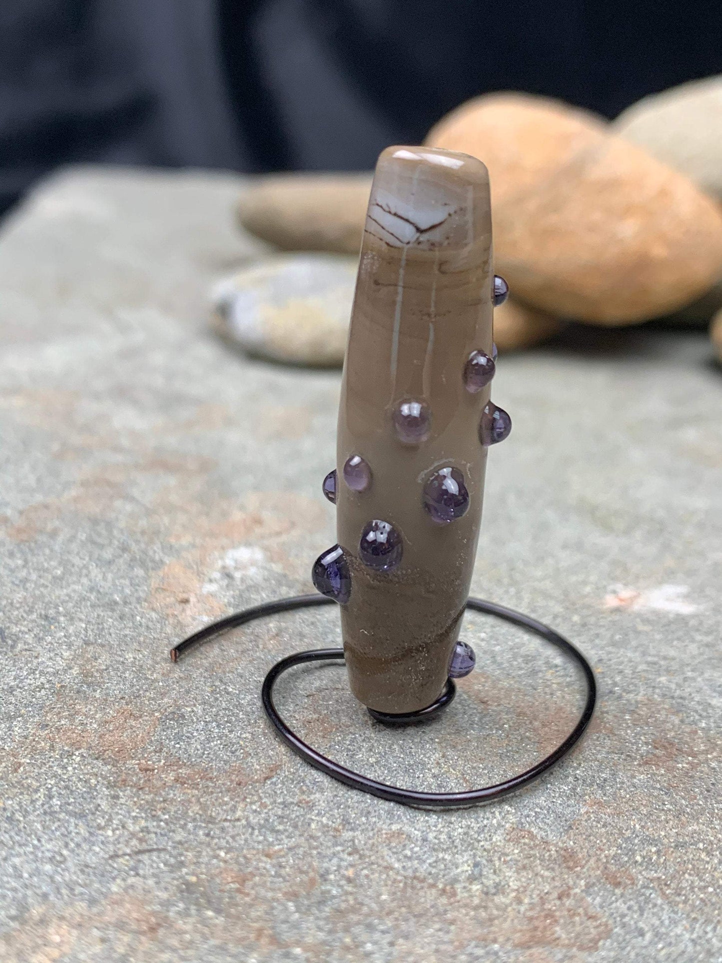 a handmade lampworked glass bead with purple dots on sage gray background