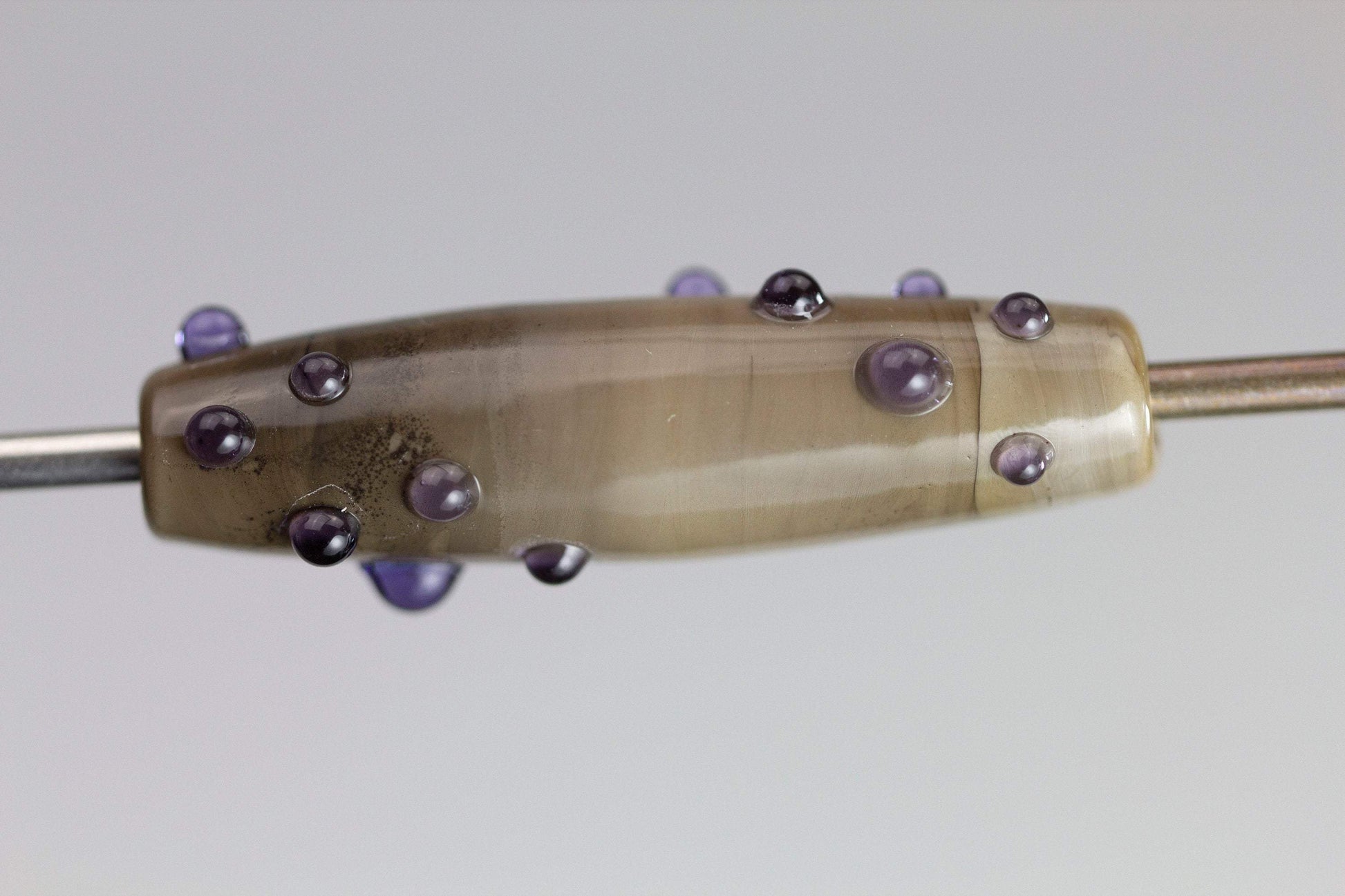 a handmade lampworked glass bead with purple dots on sage gray background