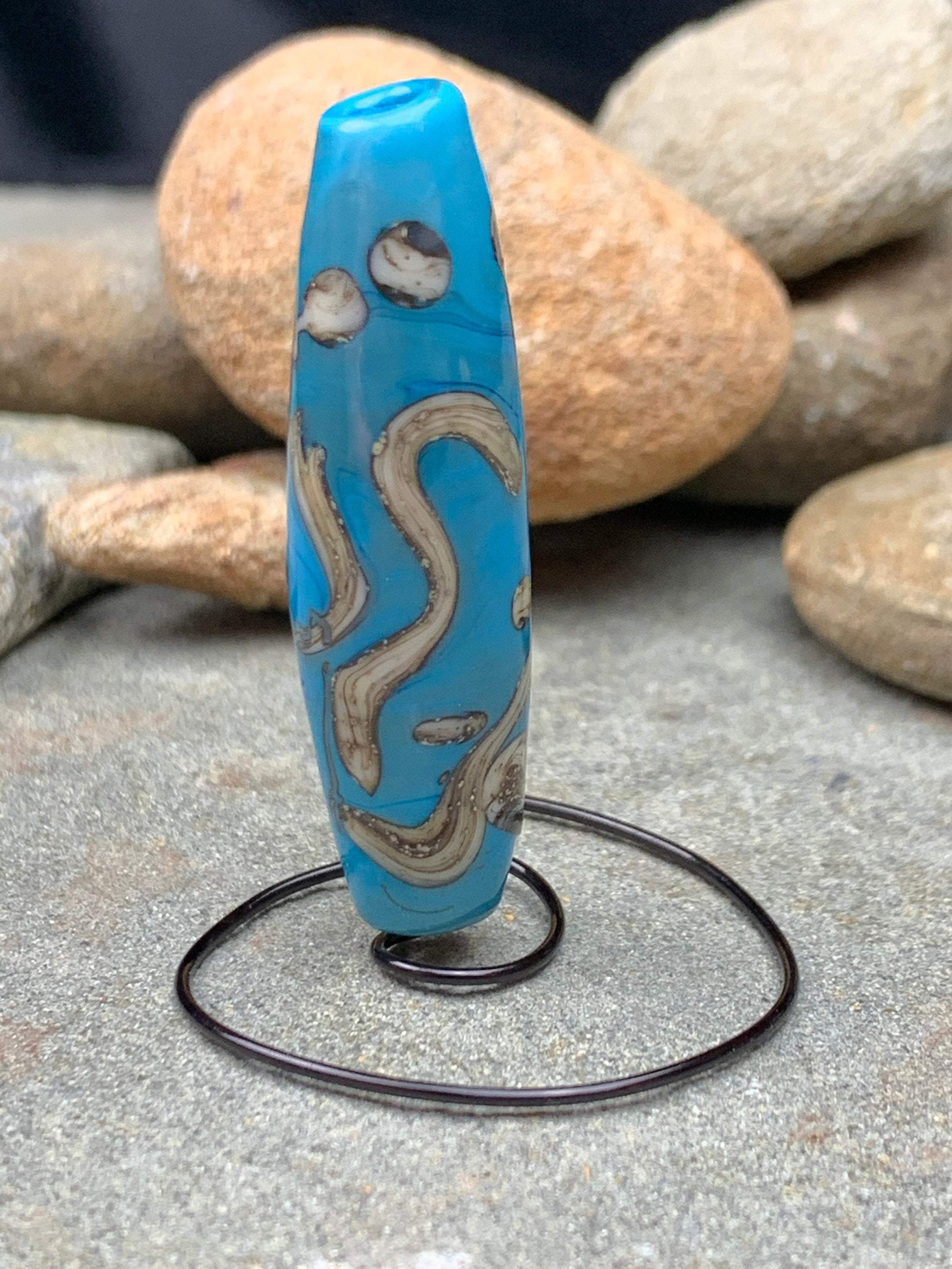 a handmade lampworked glass bead with silver and ivory swirls on a turquoise background