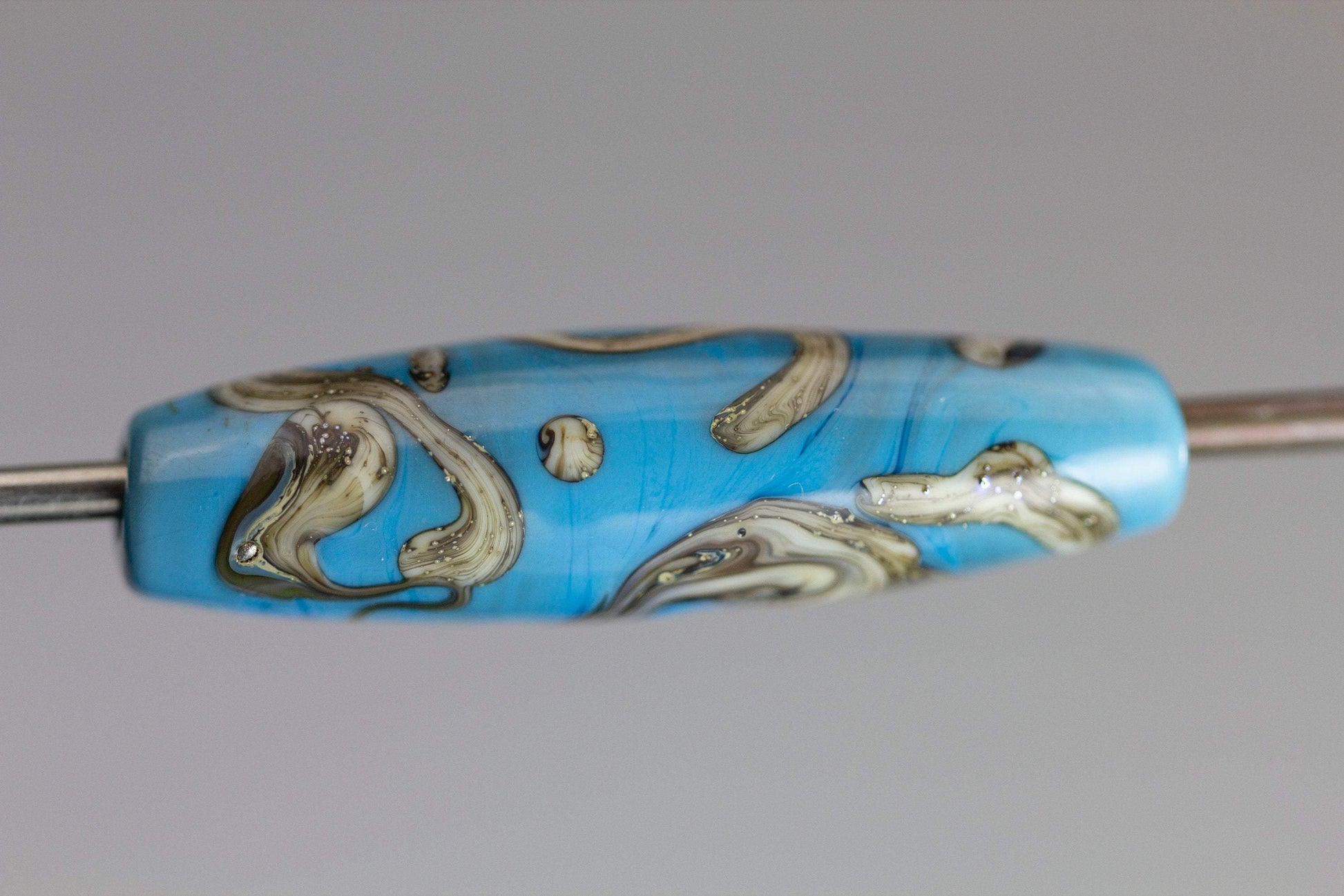 a handmade lampworked glass bead with silver and ivory swirls on a turquoise background