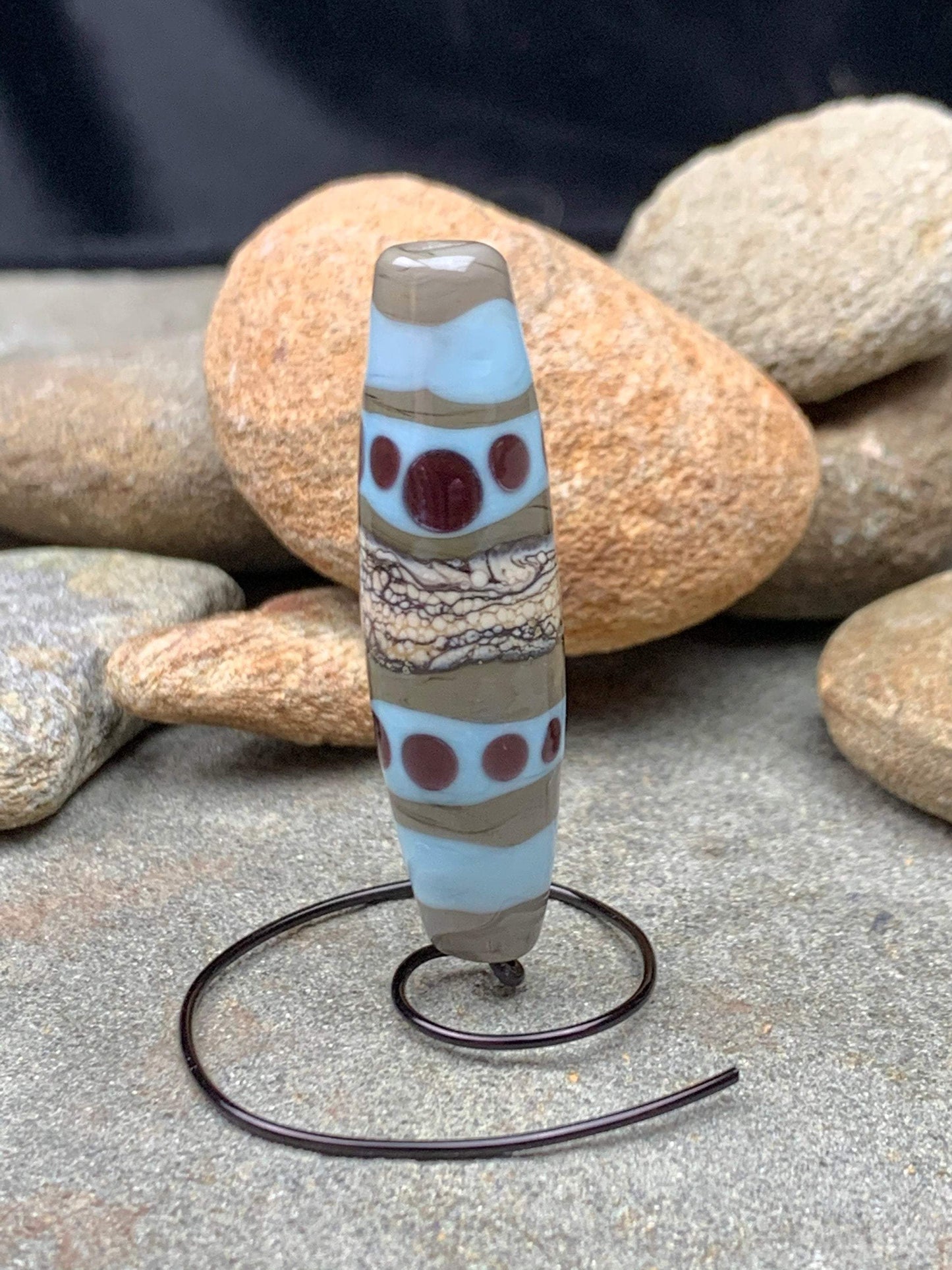 a handmade lampworked glass bead with purple dots and ivory and turquoise bands on a gray background
