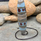a handmade lampworked glass bead with purple dots and ivory and turquoise bands on a gray background
